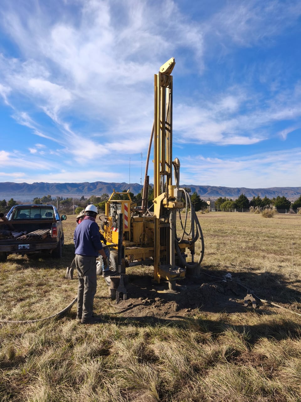 Yellow drilling rig at work on a piece of land with the sierras behind